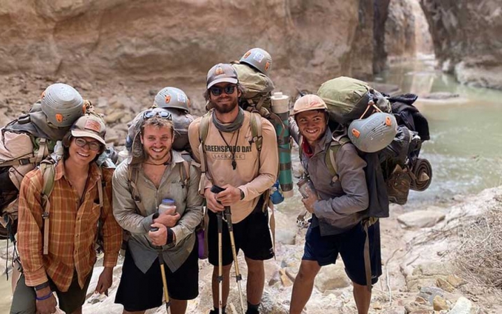 a group of gap year students wearing backpacks stand in a canyon with water in the background